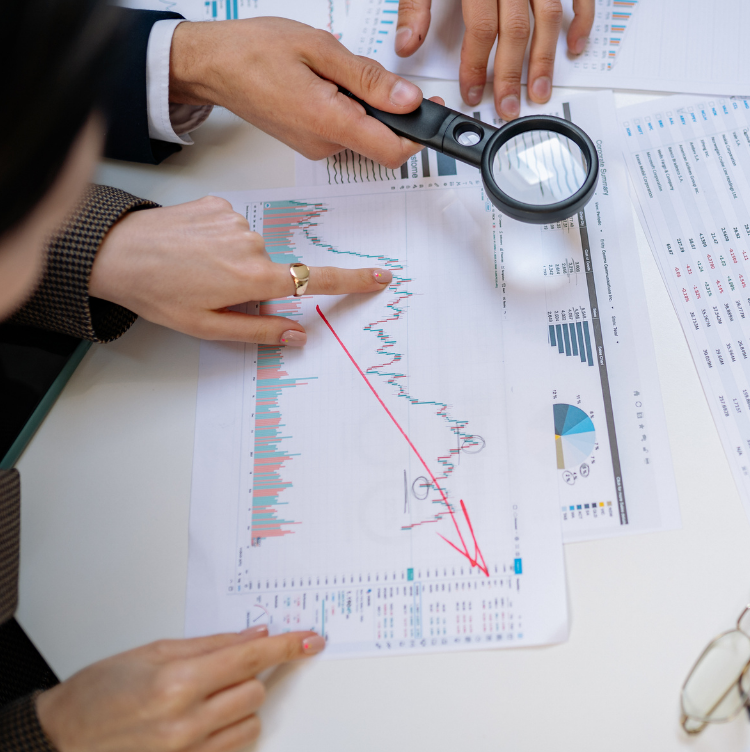 People's hands holding a magnifying glass looking at important papers